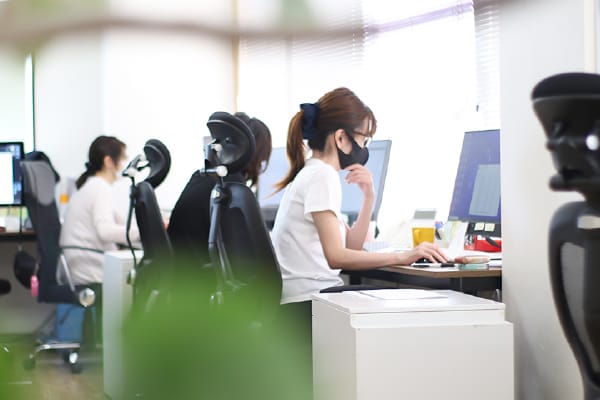 2人の女性がパソコンを使って作業をしており、1人が画面を指さしながら説明をしています。