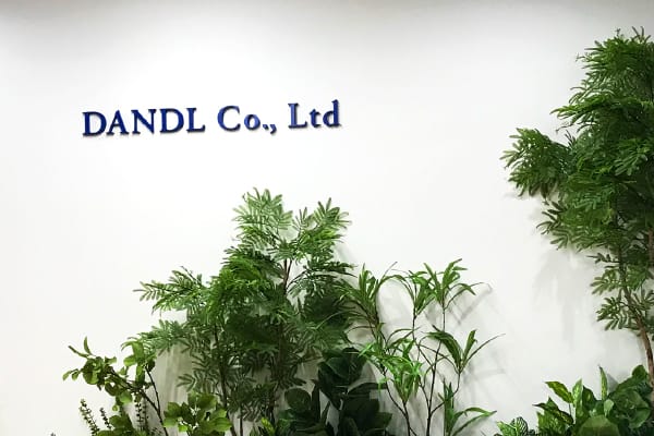 会社のロビーにあるソファとテーブル、背景には植物が飾られており、棚には多くのファイルボックスが並んでいます。