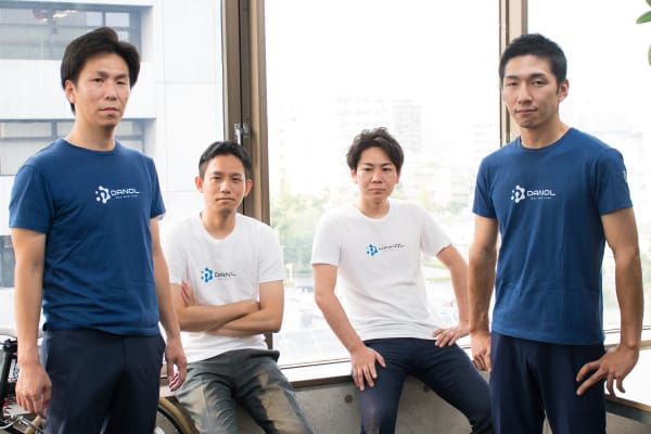  複数の人が会議室のテーブルで打ち合わせをしており、テーブルの上にはノートパソコンや書類が置かれています。